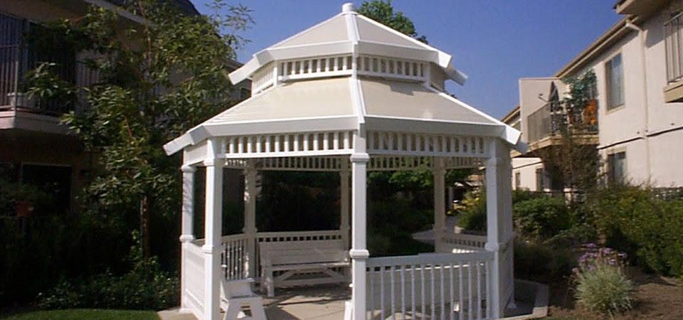 White-railed gray deck attached to a teal house, with a diagonal edge and steps off to a dirt yard