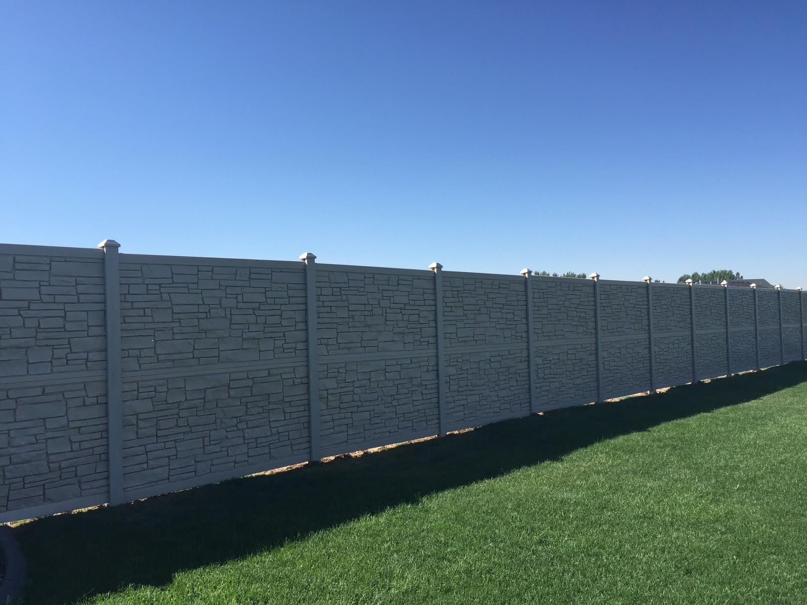 Long concrete fence along a green lawn under a clear blue sky