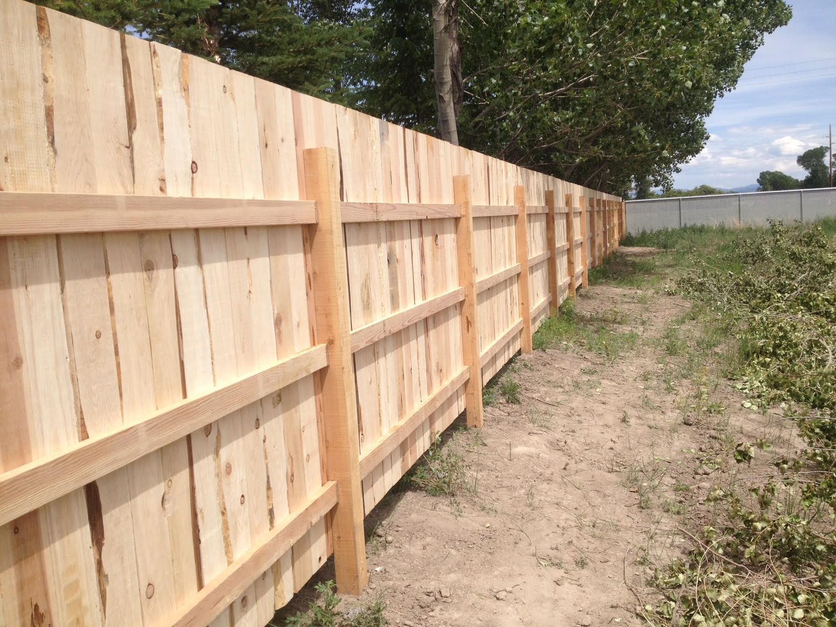 Wooden privacy fence along a grassy yard beside a house, with gray trim and corner posts.
