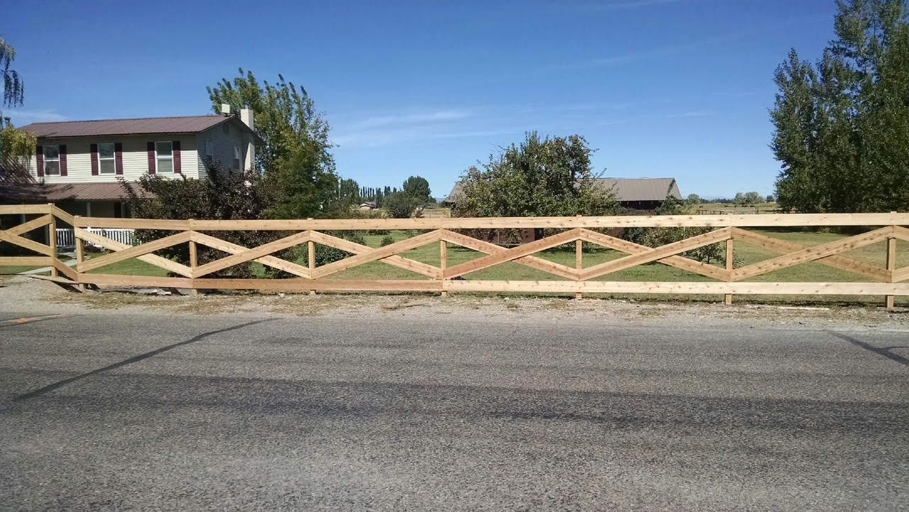 Wooden lattice fence beside a paved road, with houses and trees under a clear blue sky.