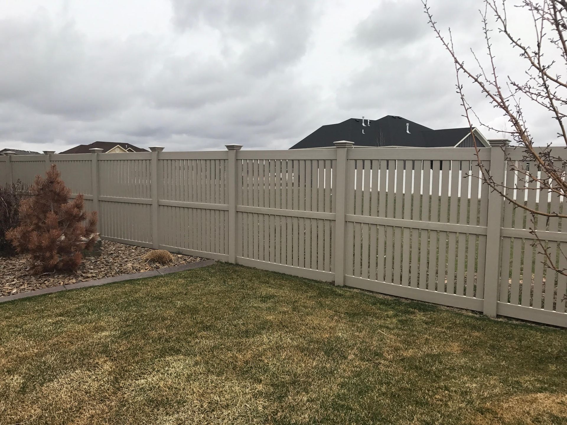 Backyard with beige fence, cloudy sky, and distant hills