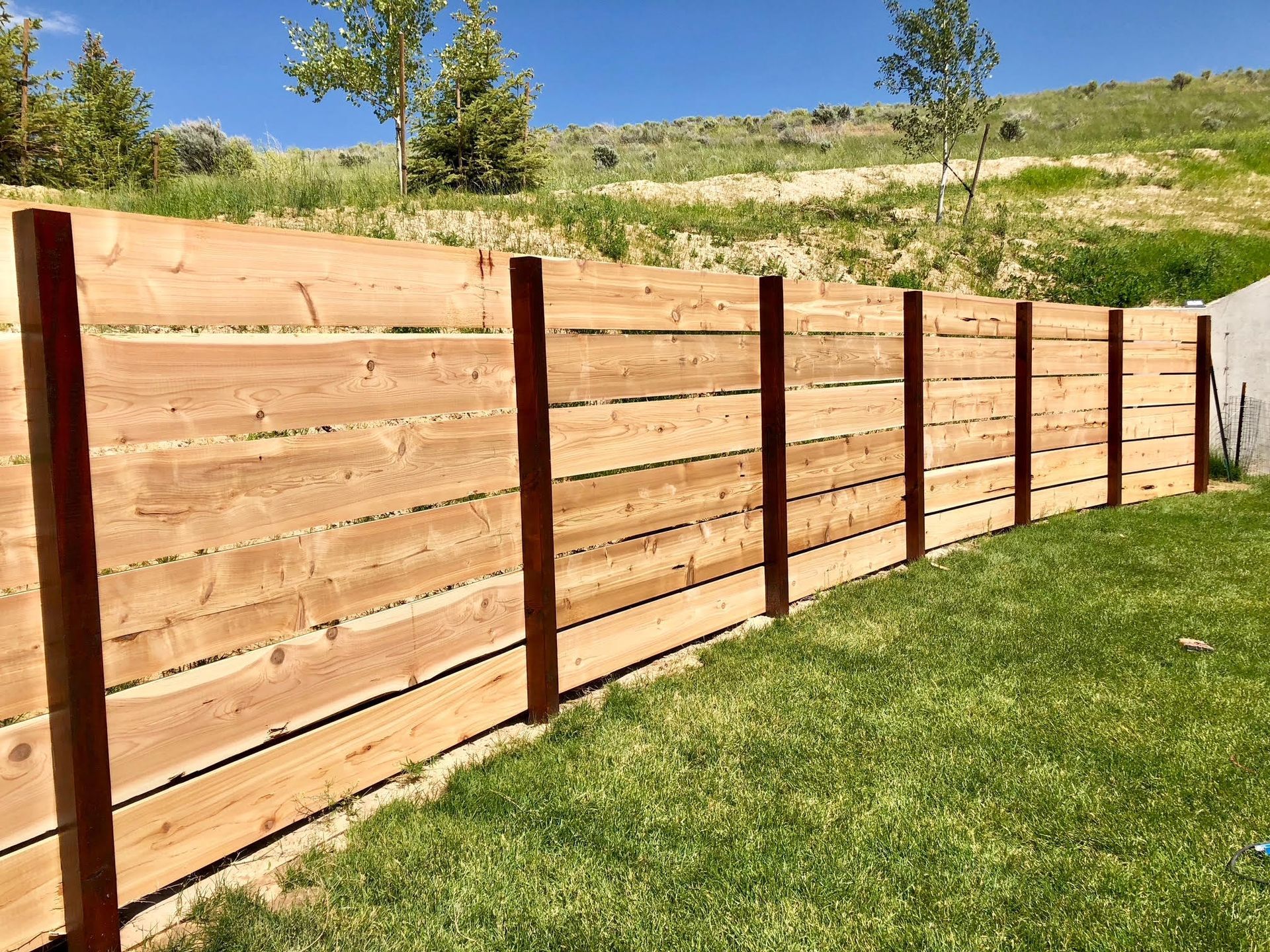 Wooden privacy fence along a grassy yard beside a house, with gray trim and corner posts.