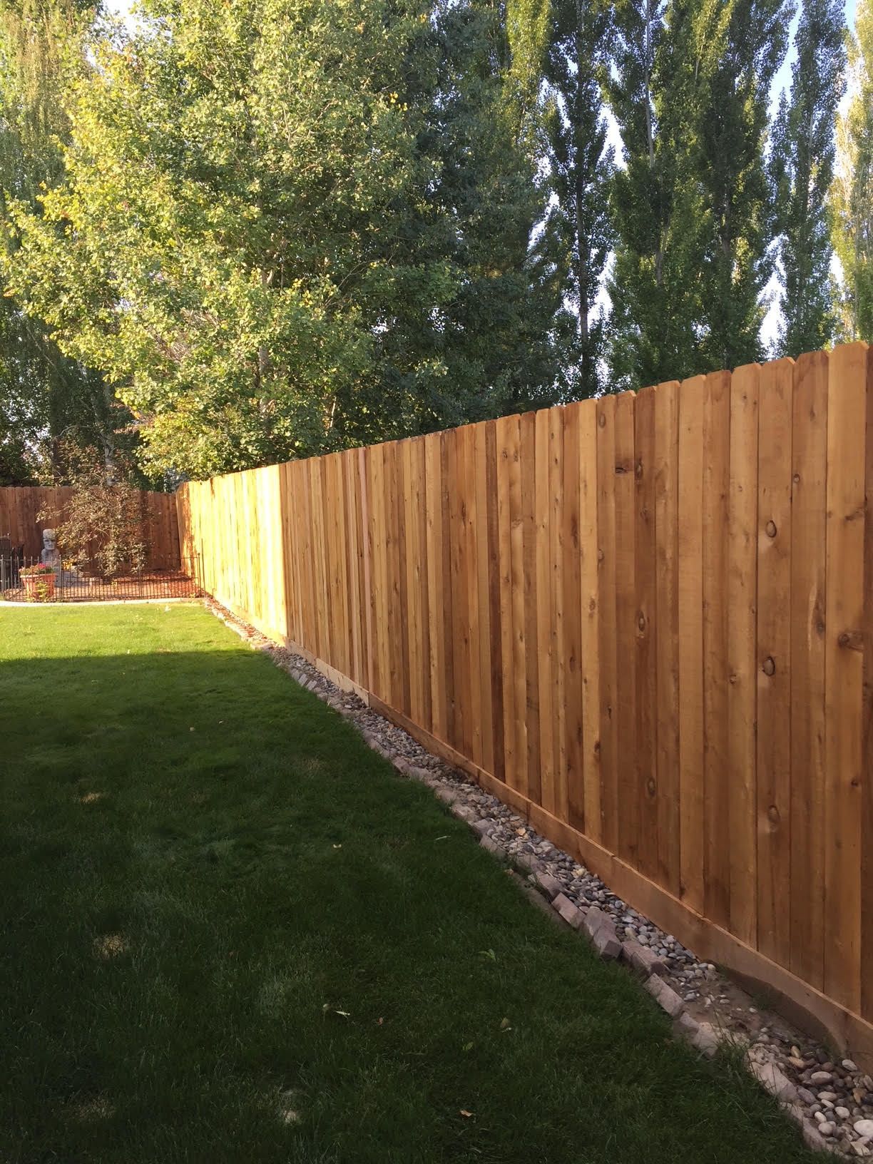 Long wooden fence beside a green lawn with trees in the background
