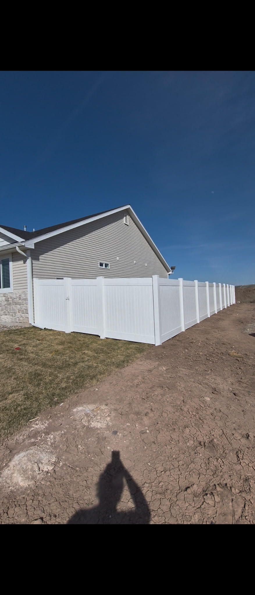 White fence panels beside a house under construction on a dirt lot under a clear blue sky