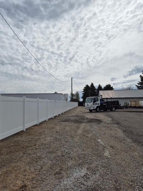 Gravel lot beside a white fence and parked trucks under a cloudy sky