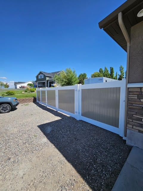 White vinyl fence beside a house and gravel driveway under a clear blue sky