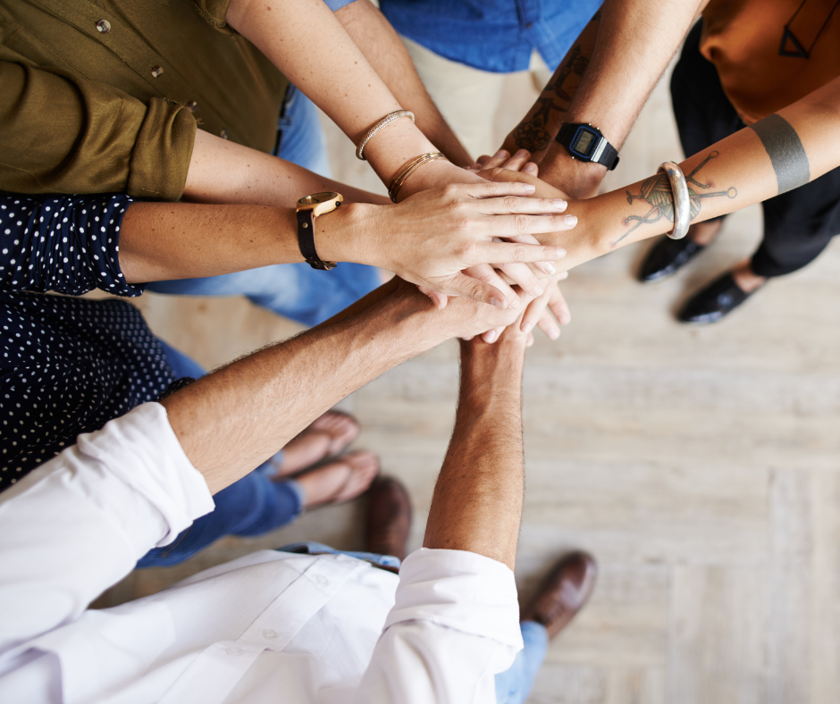 Group of coworkers stacking hands in a teamwork huddle on a wooden floor