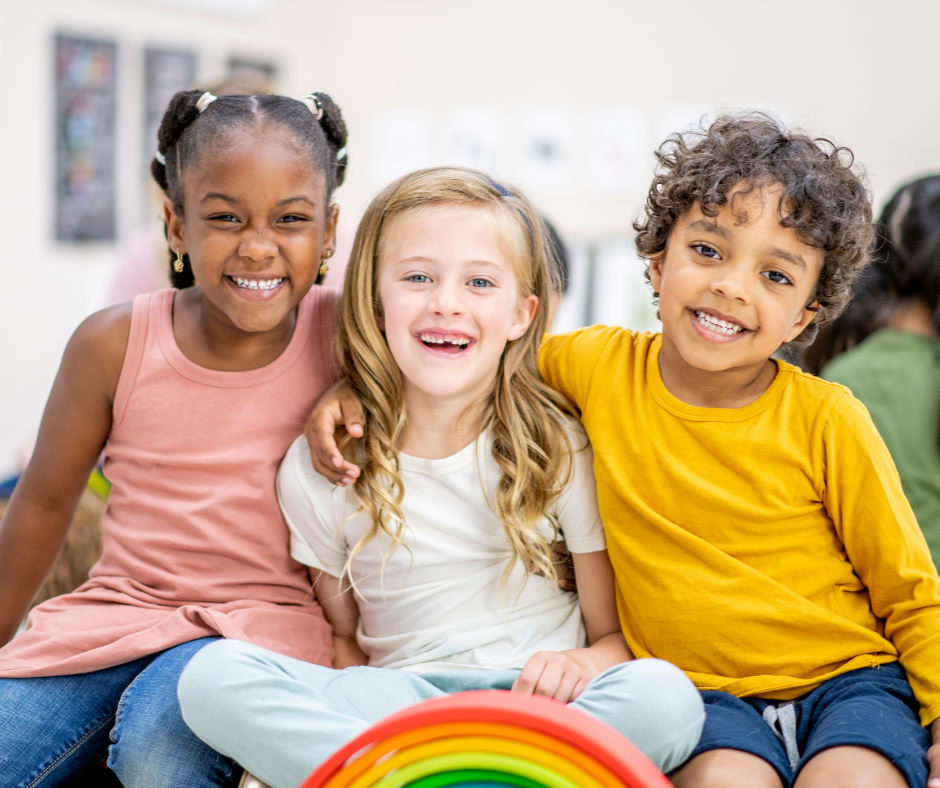 Three smiling children sitting together, with a rainbow toy in front of them.