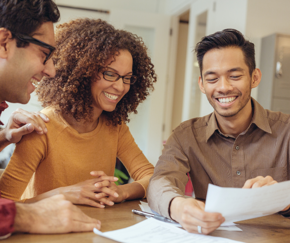 Three colleagues smiling and reviewing documents together at a table in a bright office
