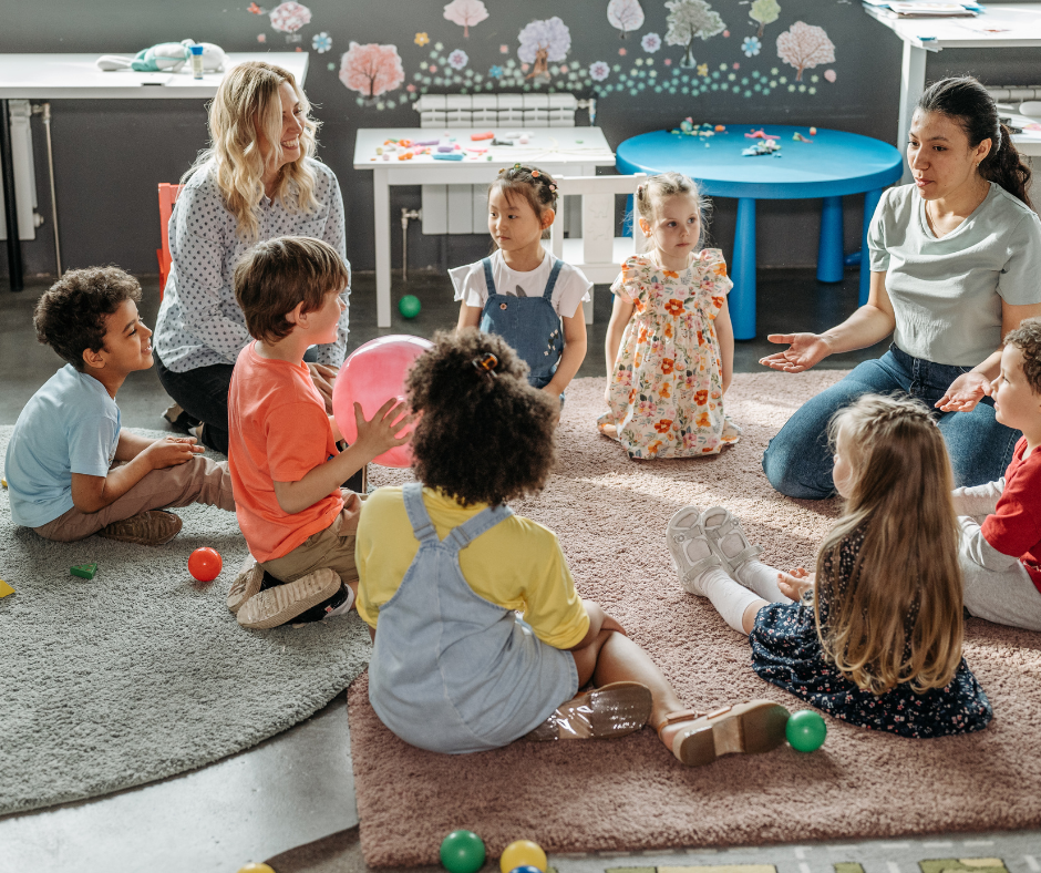 Children and adults sitting in a circle on a classroom floor, playing with colorful balls and listening together.