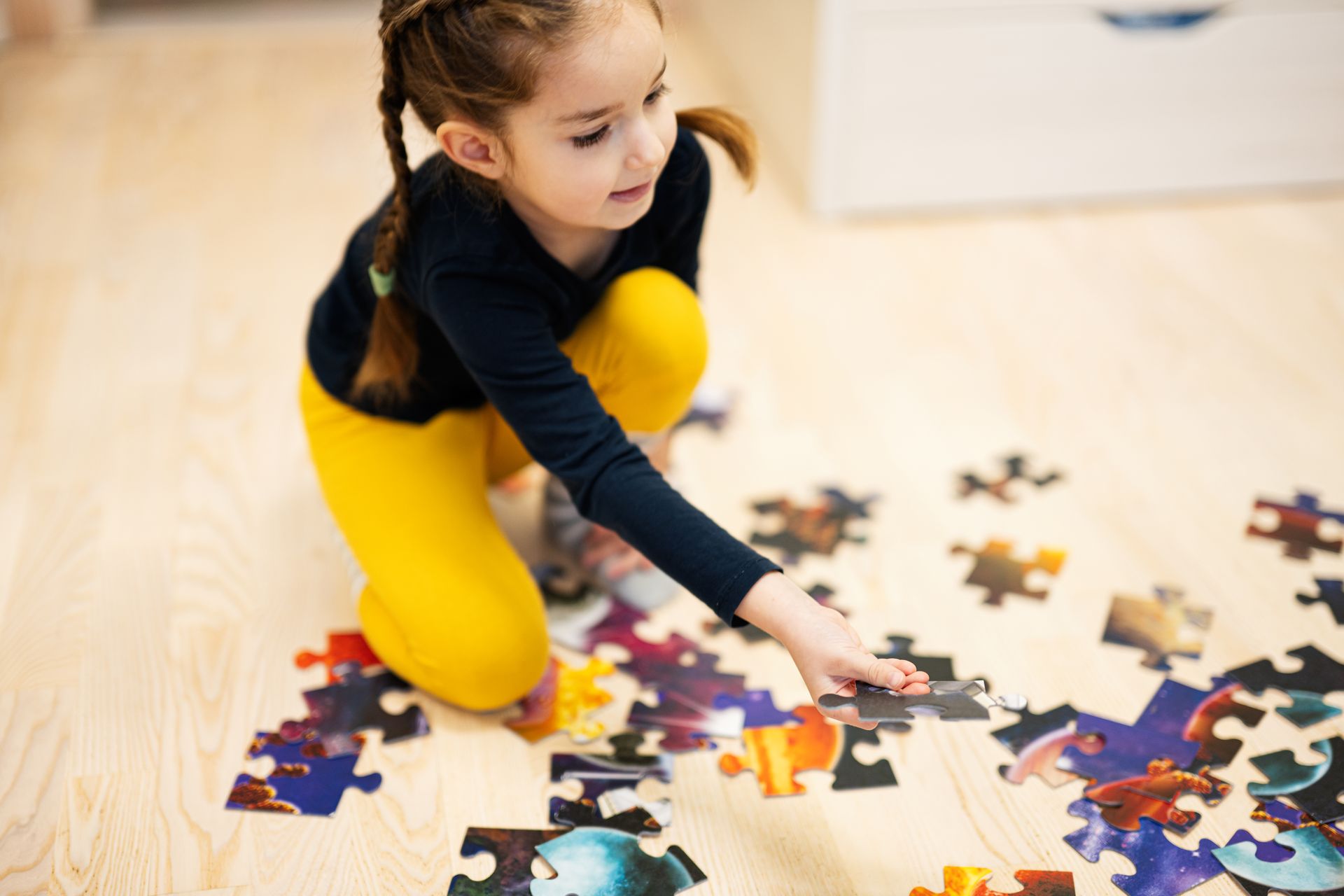 Child kneeling on a wooden floor, fitting pieces of a colorful jigsaw puzzle