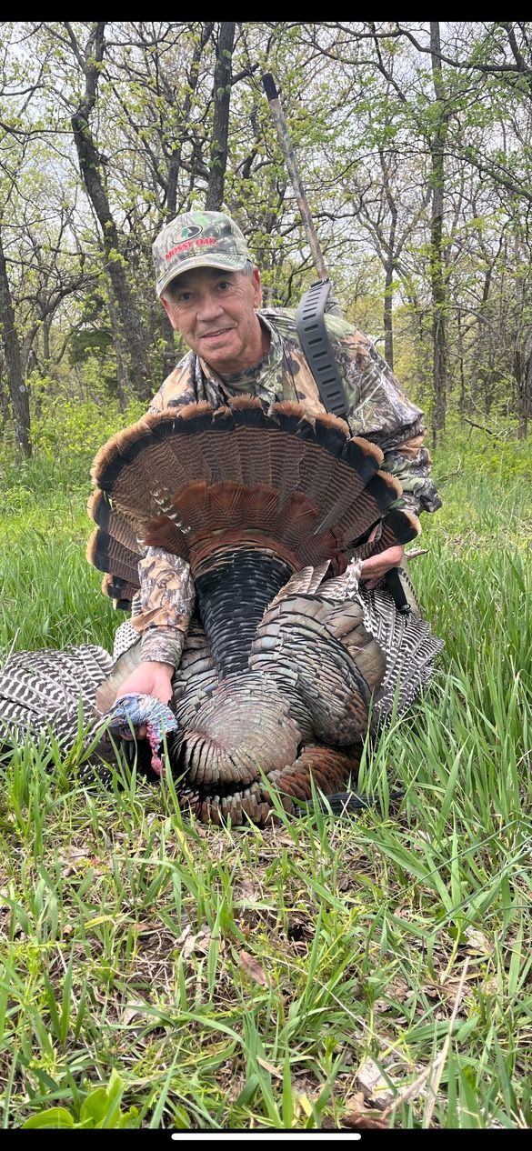 A man is holding a large Kansas turkey in a field.