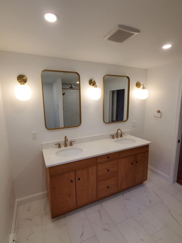 Bathroom with wood vanity, two mirrors, and gold sconces on white walls.