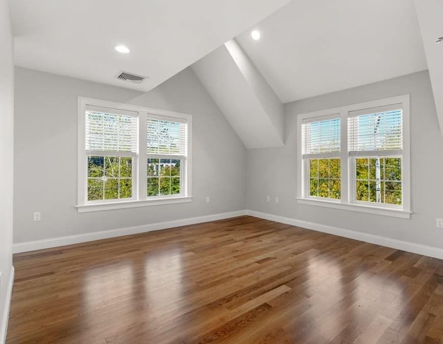 Empty bedroom with hardwood floors, two windows with blinds, and slanted ceiling.