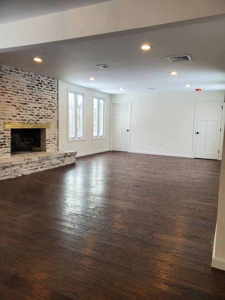 Empty living room with dark wood floor, white walls, fireplace, and doors.