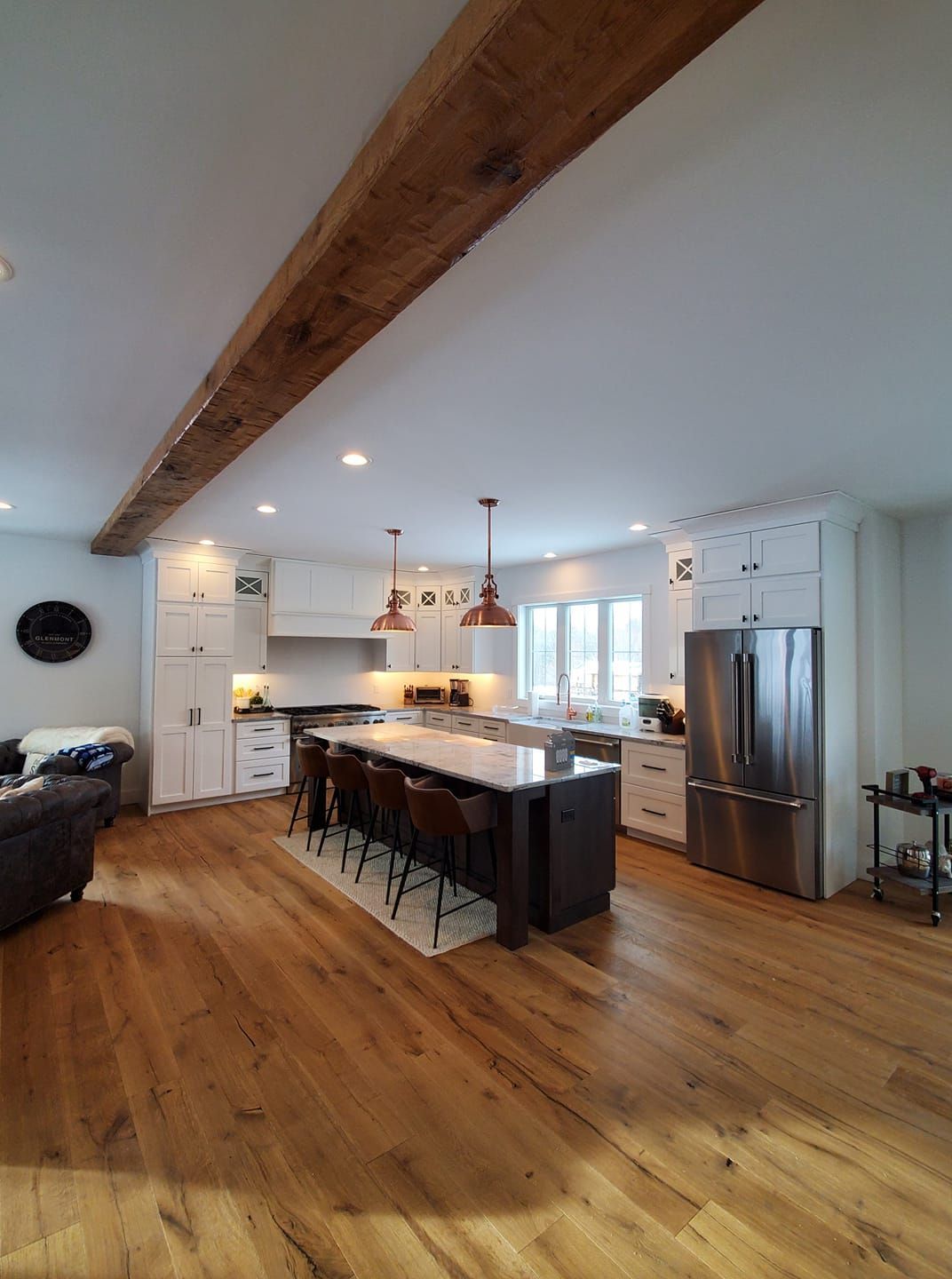Open-concept kitchen with wooden floors, island with seating, white cabinets, and a wooden beam across the ceiling.