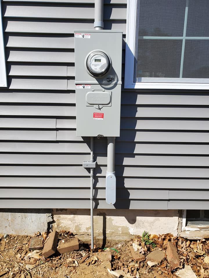 Gray electrical meter box on a gray house with a grounding rod, located next to a window.