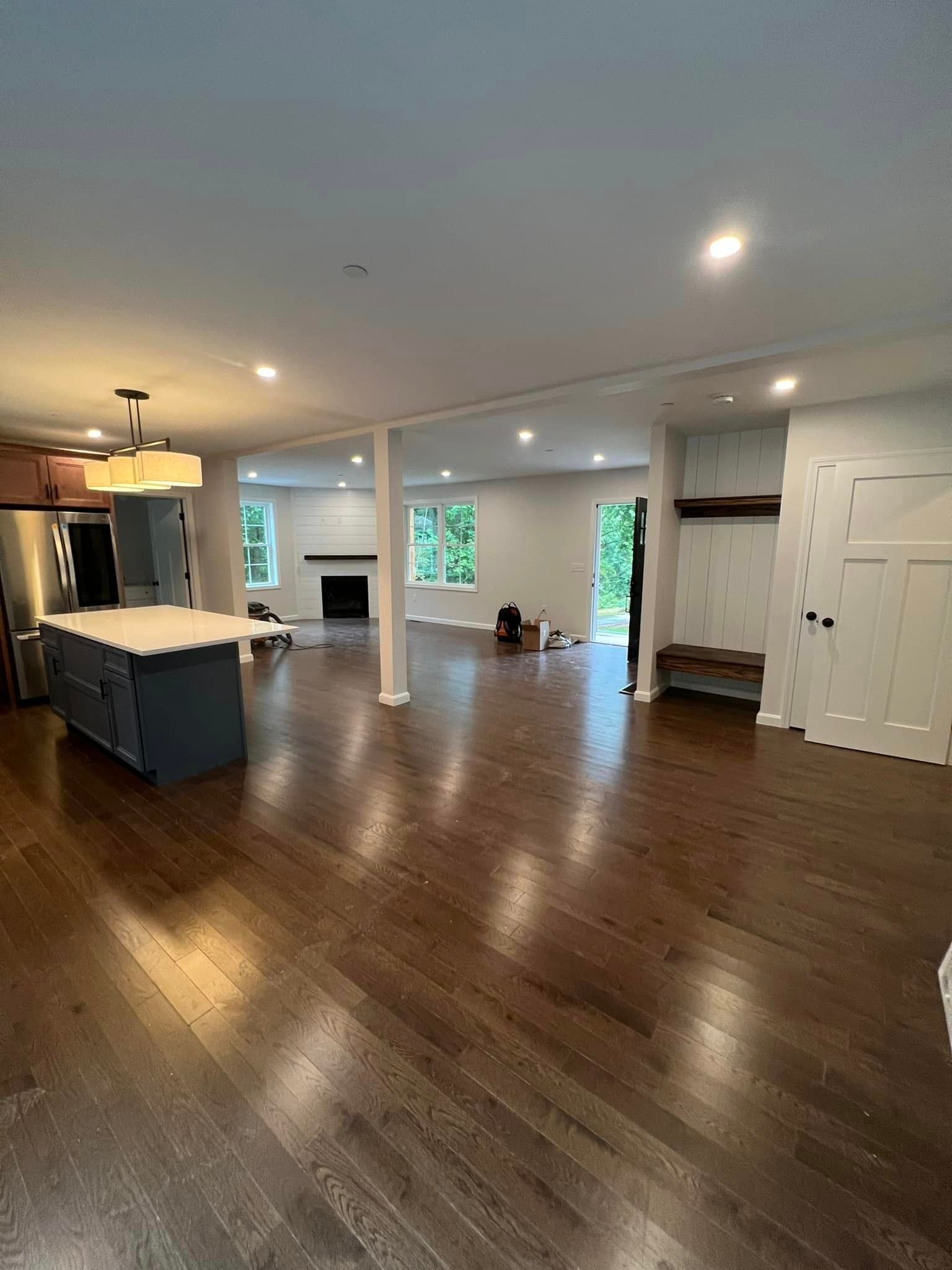 Open-concept living space with dark wood floors, white walls, kitchen island, and fireplace.