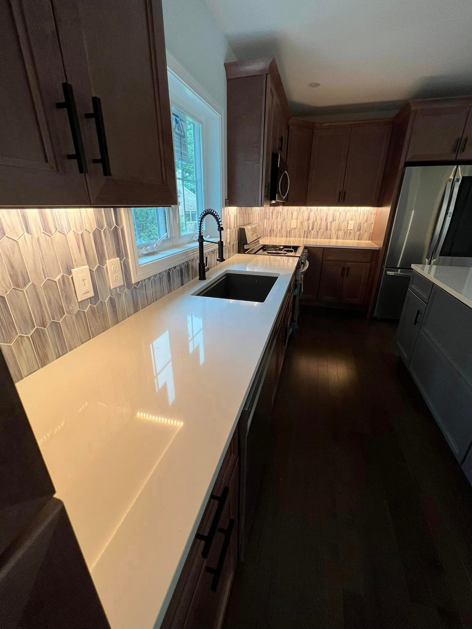 Long countertop and cabinets in a kitchen, with backsplash and dark sink.
