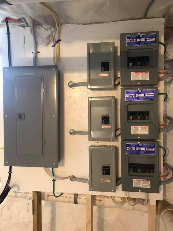 Electrical panel board with multiple subpanels mounted on a white wall in a basement.