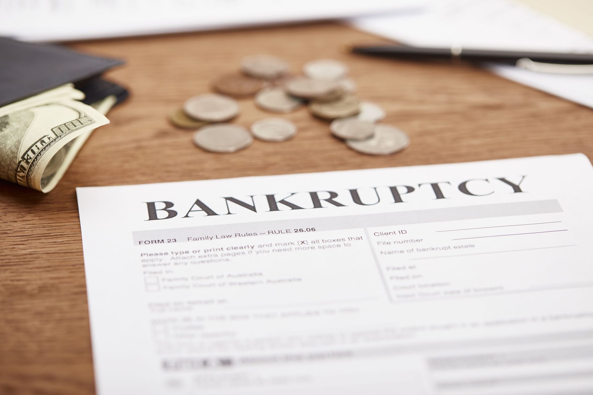 Bankruptcy form on a wooden desk with scattered coins and a rolled dollar bill