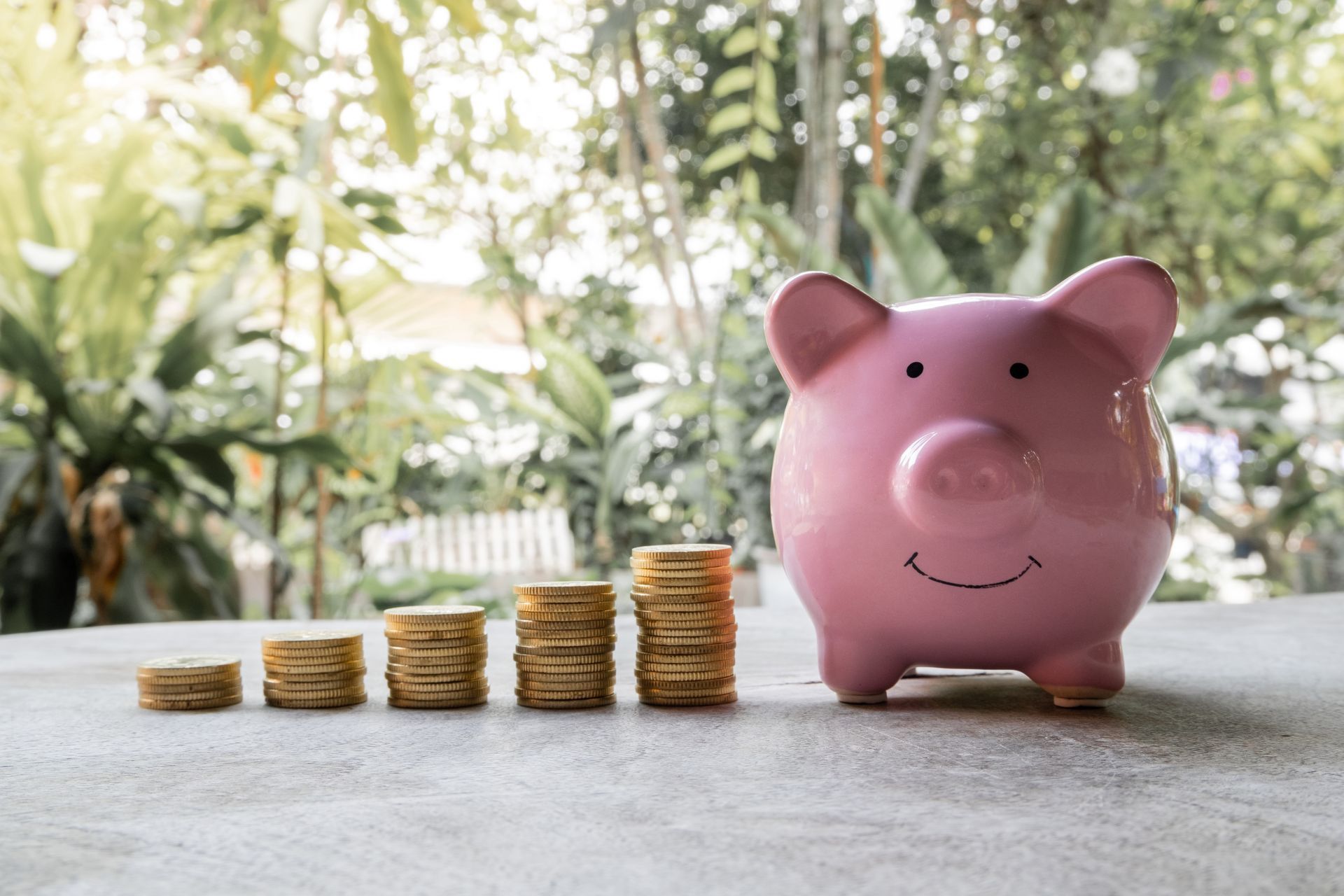 A pink piggy bank sitting next to stacks of coins on a table.