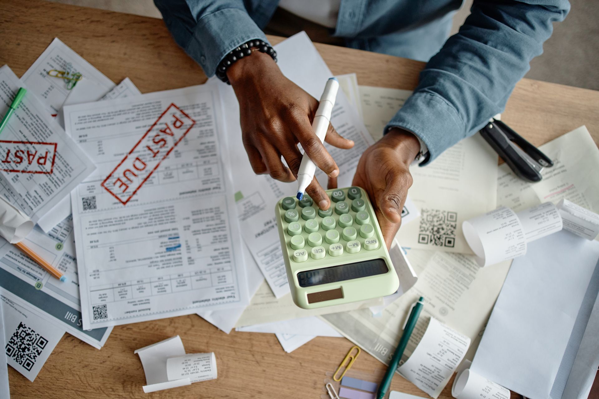 Person calculating bills with a calculator, surrounded by paperwork, including a 