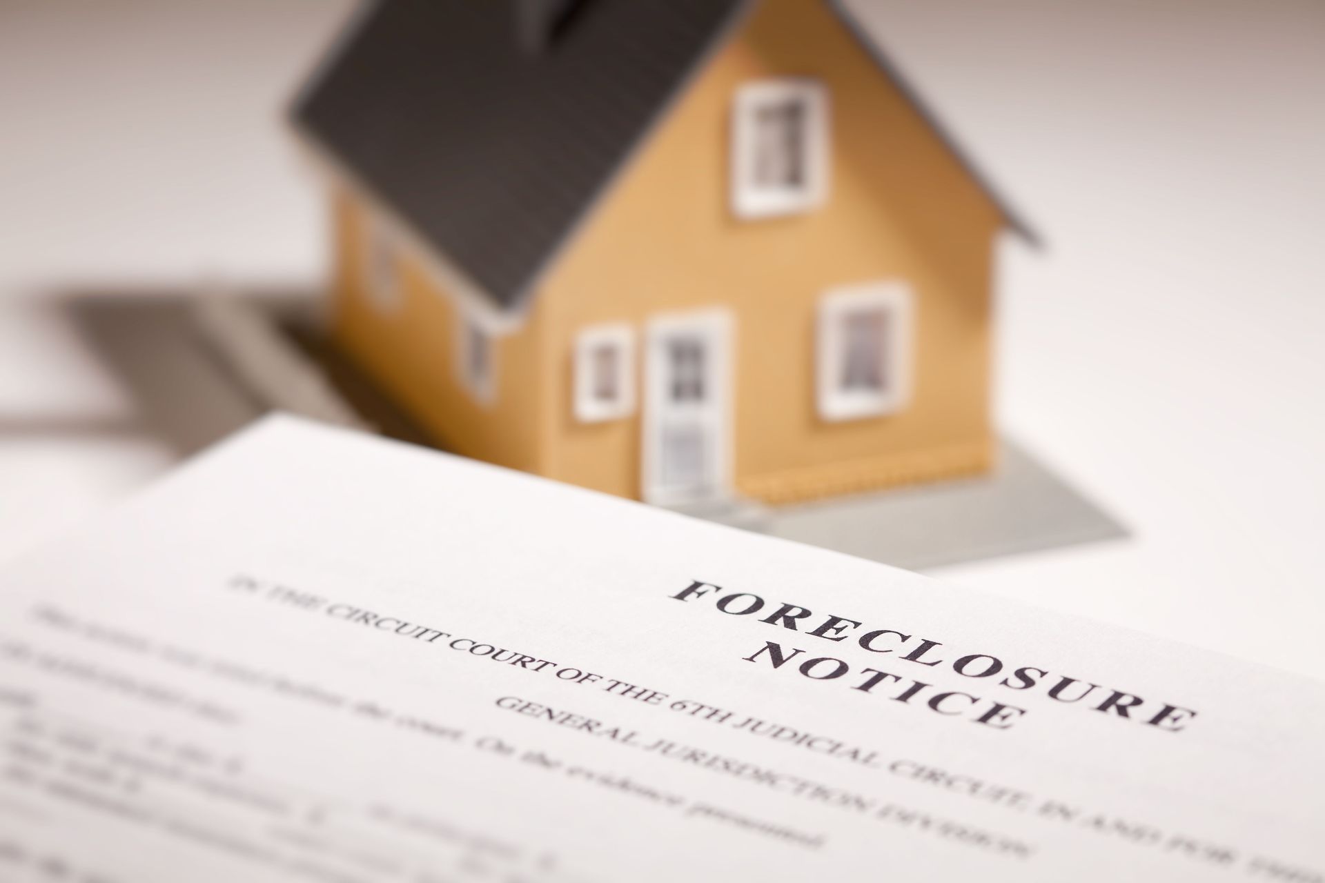 Foreclosure notice document in focus, with toy house blurred in background.