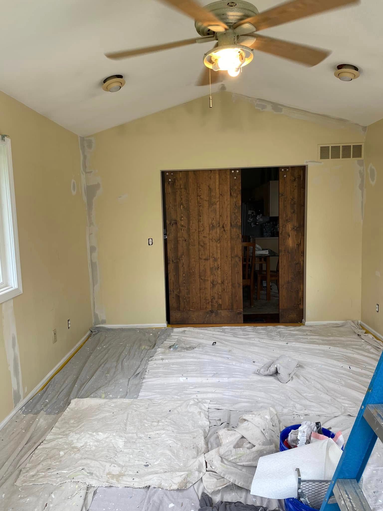 A room that is being painted with a ceiling fan.