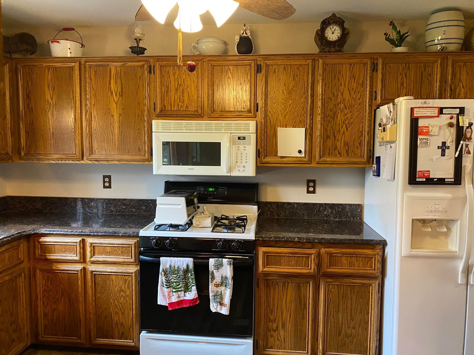 A kitchen with wooden cabinets , a stove , microwave and refrigerator.