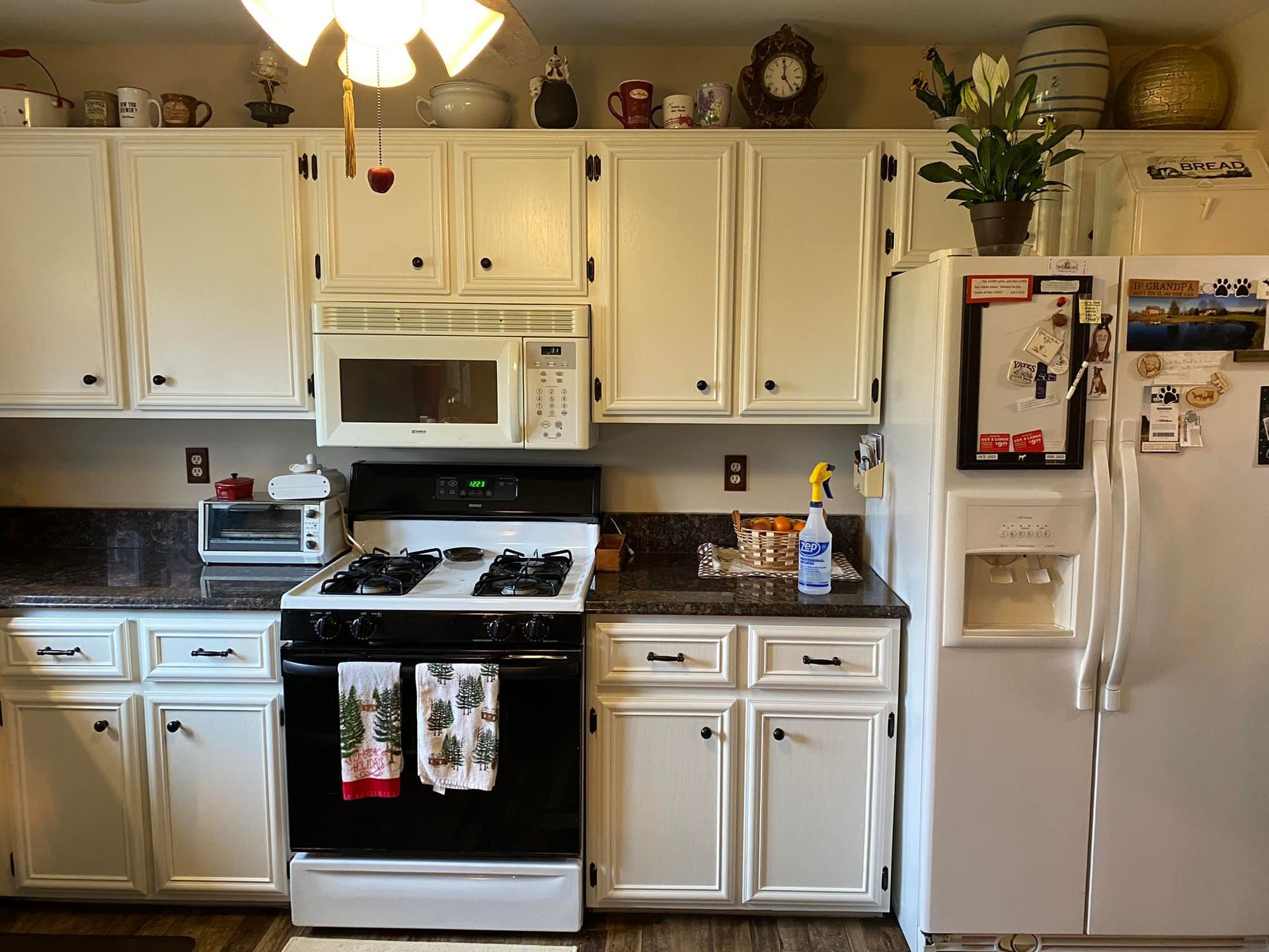 A kitchen with white cabinets , a stove , a refrigerator and a microwave.