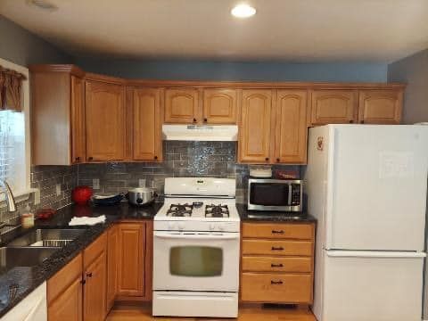 A kitchen with a stove , refrigerator , microwave and sink.