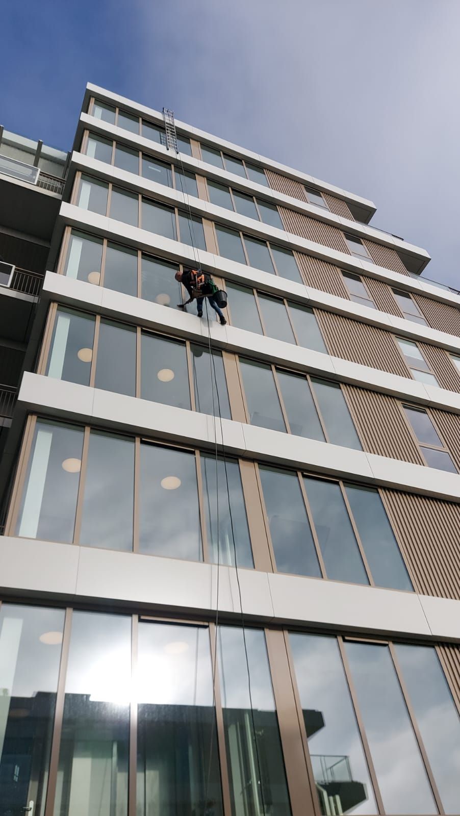 Een man maakt de ramen van een hoog gebouw schoon.