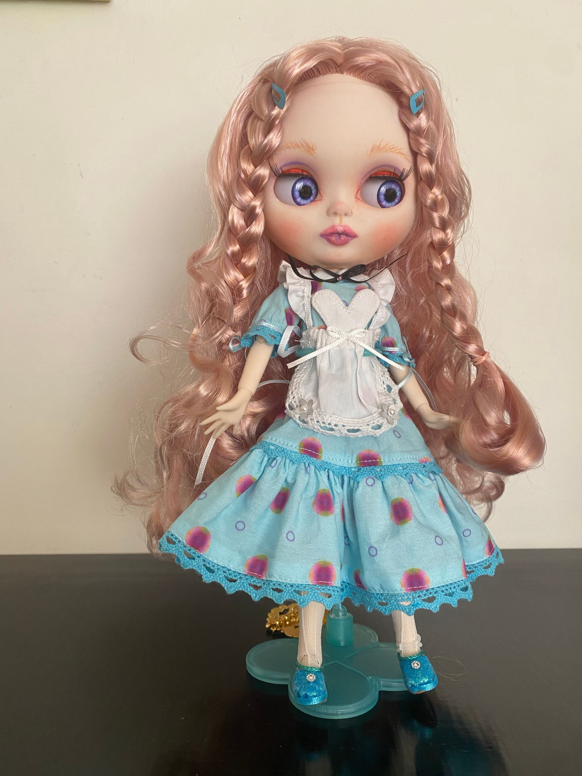 Pop in een blauwe jurk met roze haar en blauwe schoenen, op een standaard.