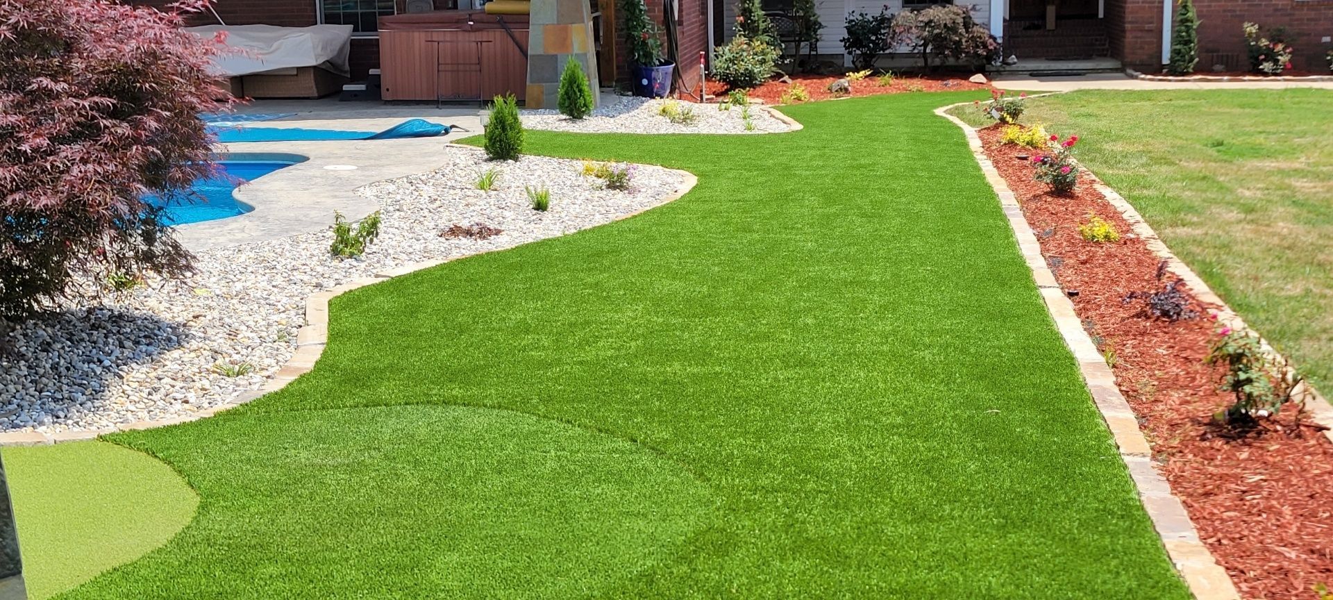 A lush green lawn in front of a house with a pool in the background.