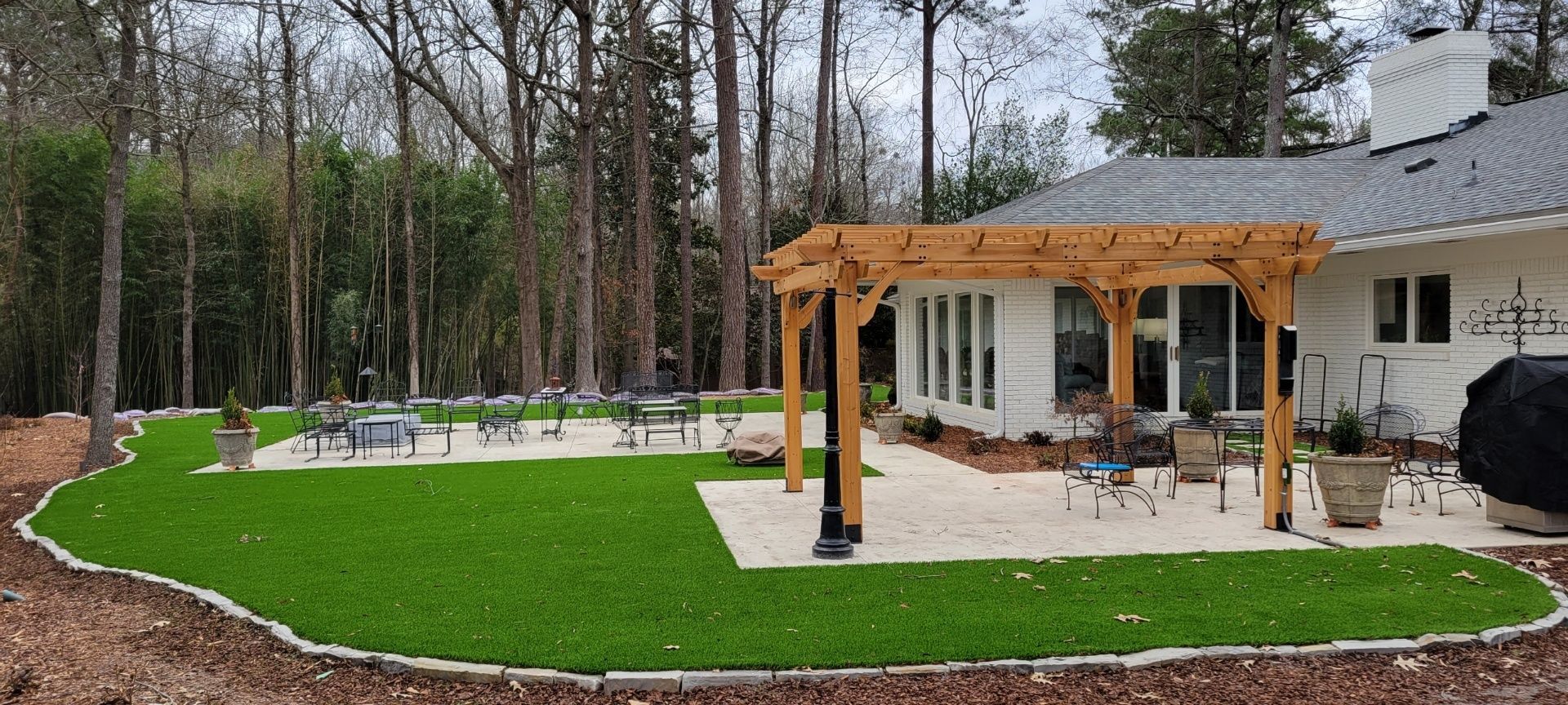 A white house with a pergola in the backyard surrounded by trees.
