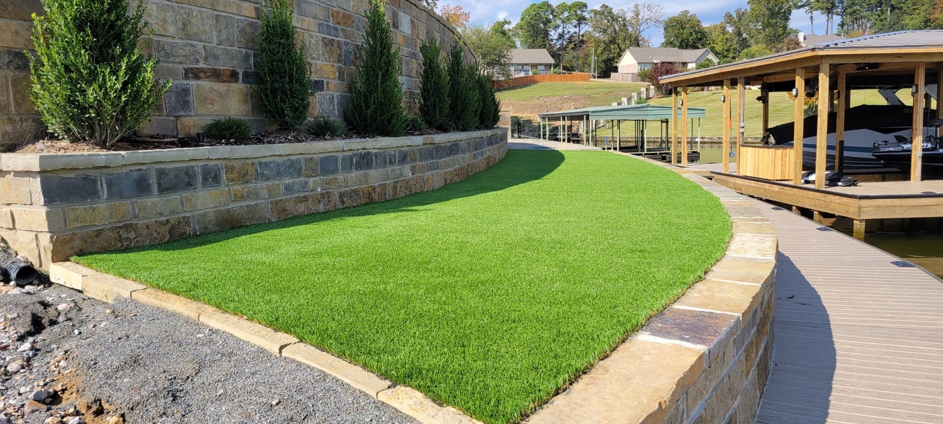 A stone wall surrounds a lush green lawn next to a dock.