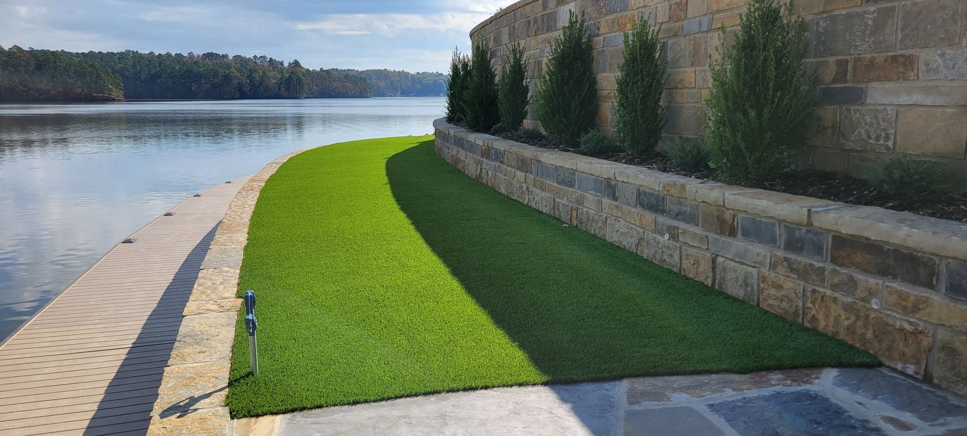 A lush green lawn next to a stone wall next to a body of water.