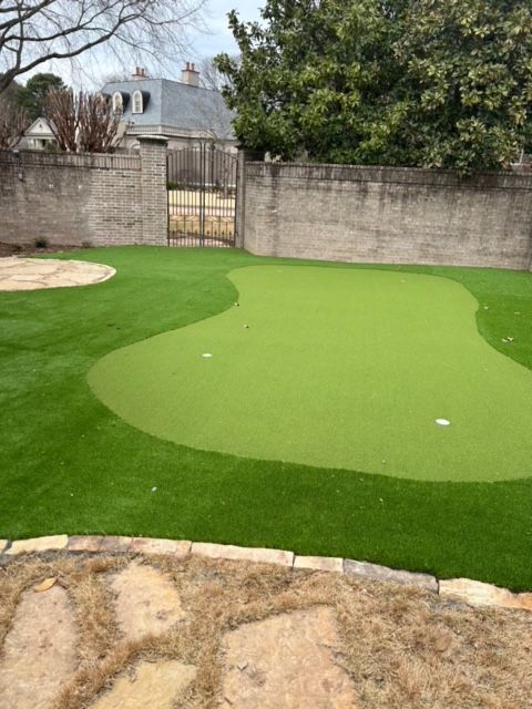 A green golf course in a backyard with a brick wall in the background.