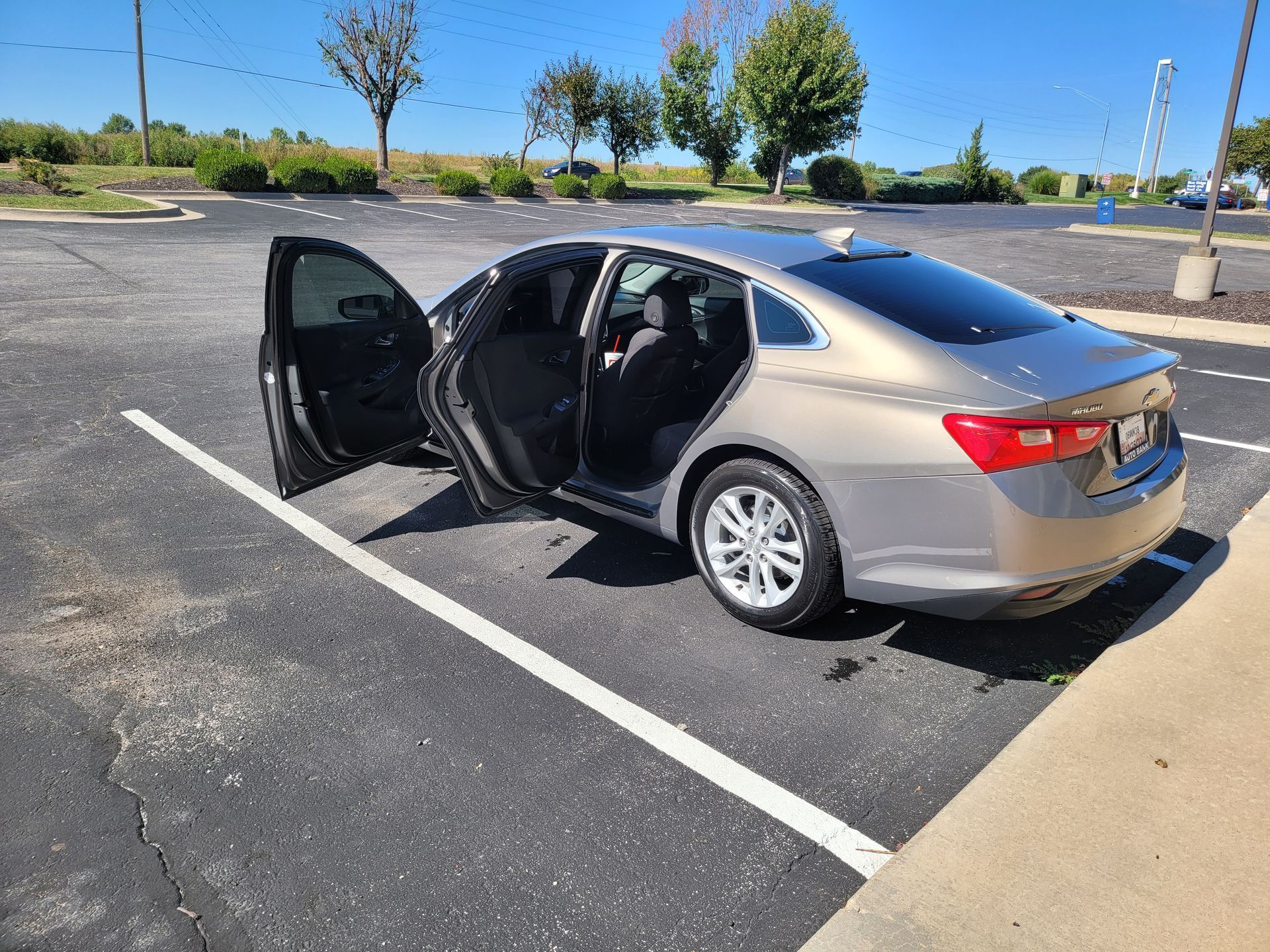 A silver car is parked in a parking lot with its doors open.