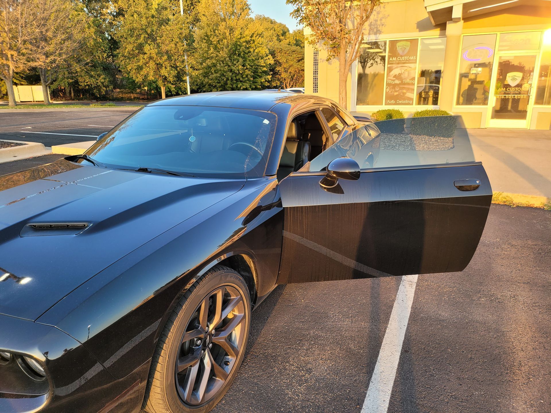 A black dodge challenger is parked in a parking lot with its doors open.