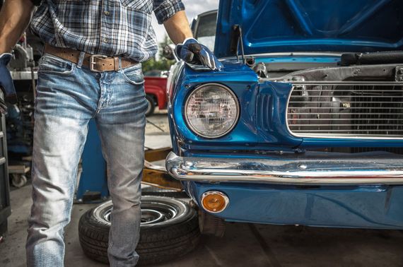 A man is working on a blue car in a garage.