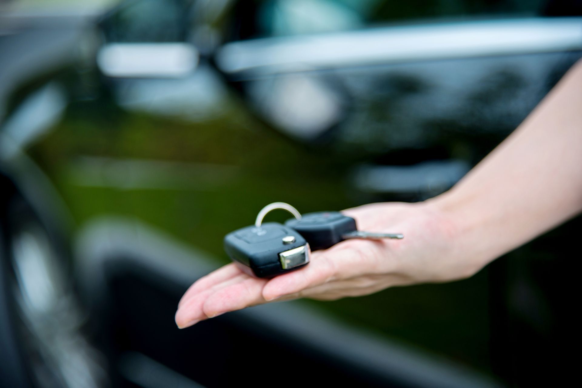 A person is holding a pair of car keys in front of a car.
