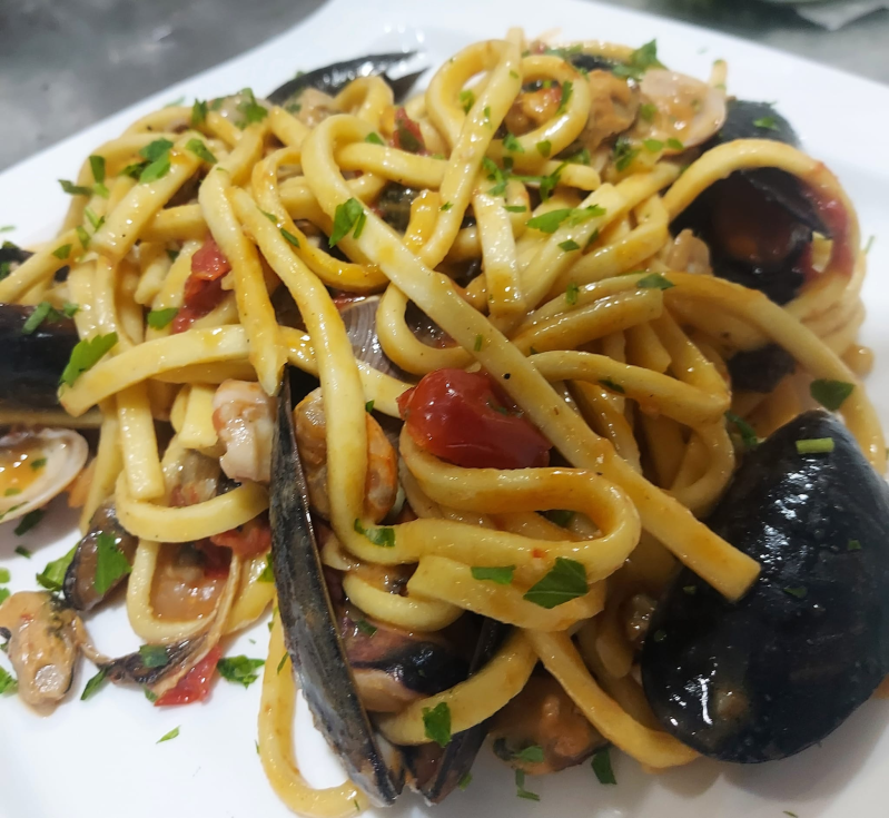 Un piatto bianco con sopra tagliatelle, cozze e pomodori
