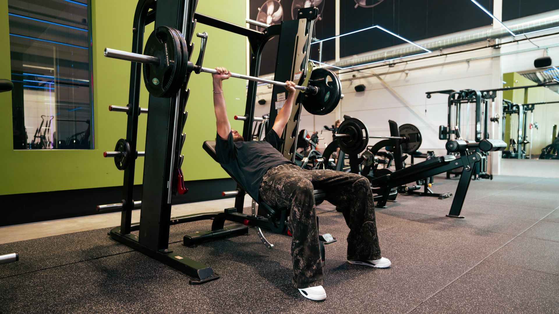 Persoon die een barbell bankdrukt in een sportschool. Groene muur, zwarte apparatuur en gewichten.