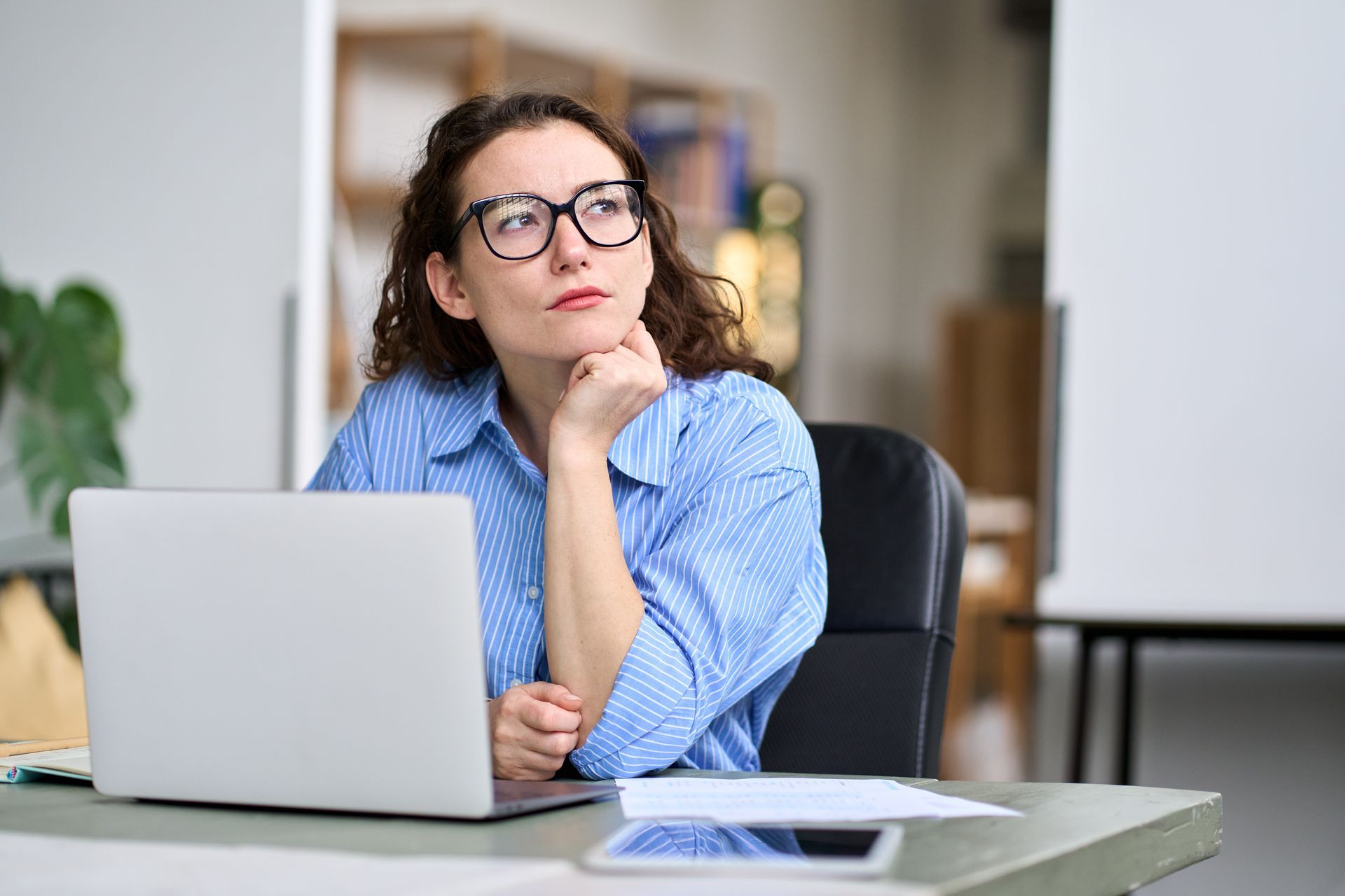 A woman is sitting at a desk in front of a laptop computer.