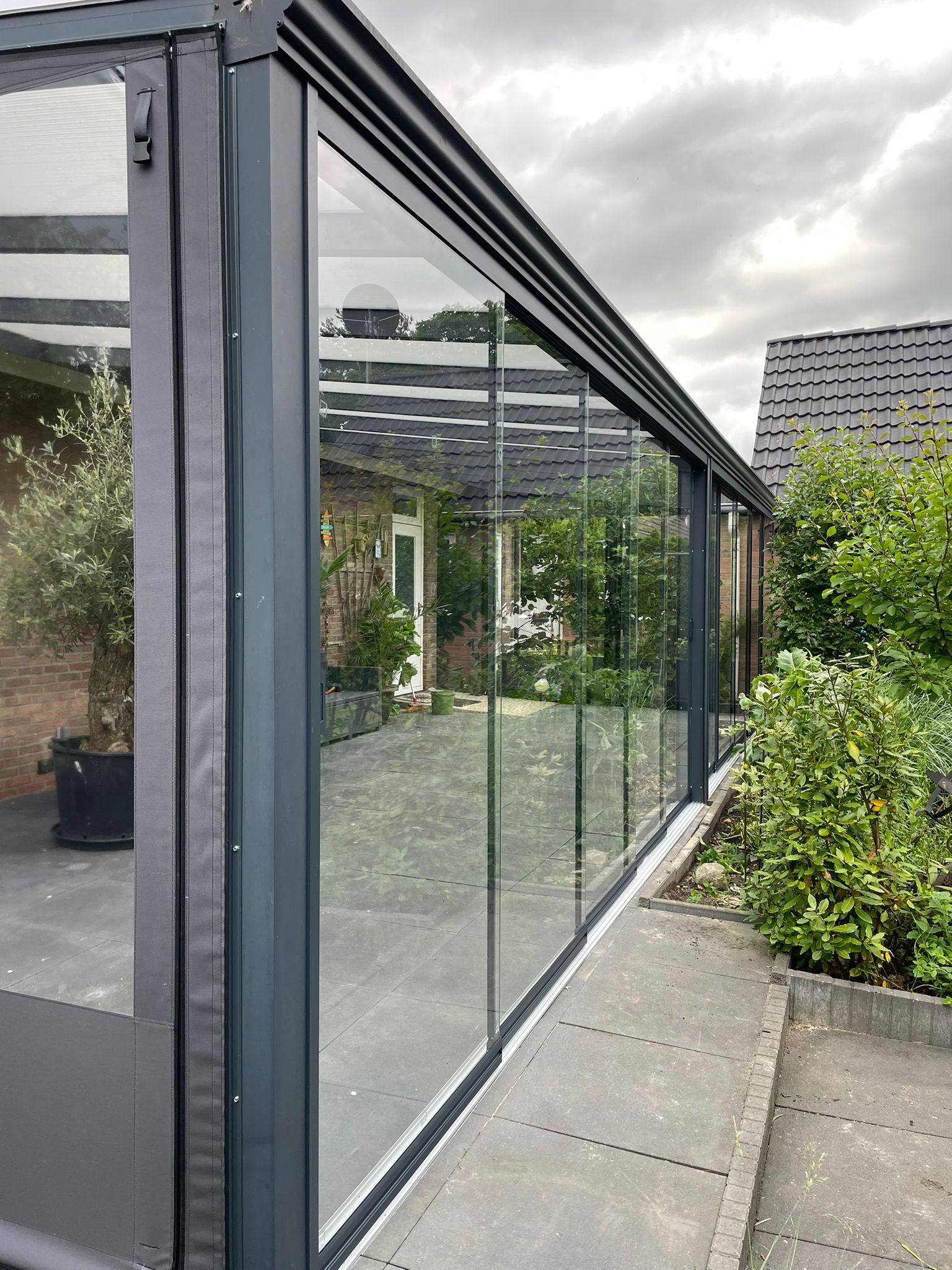 Een groot glazen gebouw met glazen schuifdeuren staat naast een huis.