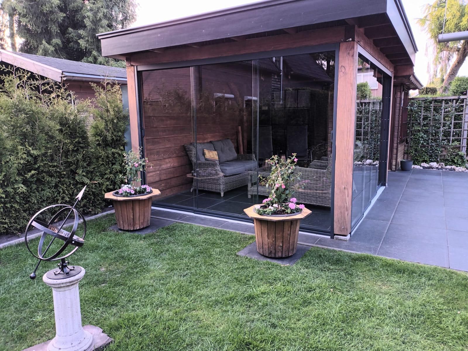 Een houten prieel met glazen schuifdeuren in een achtertuin.