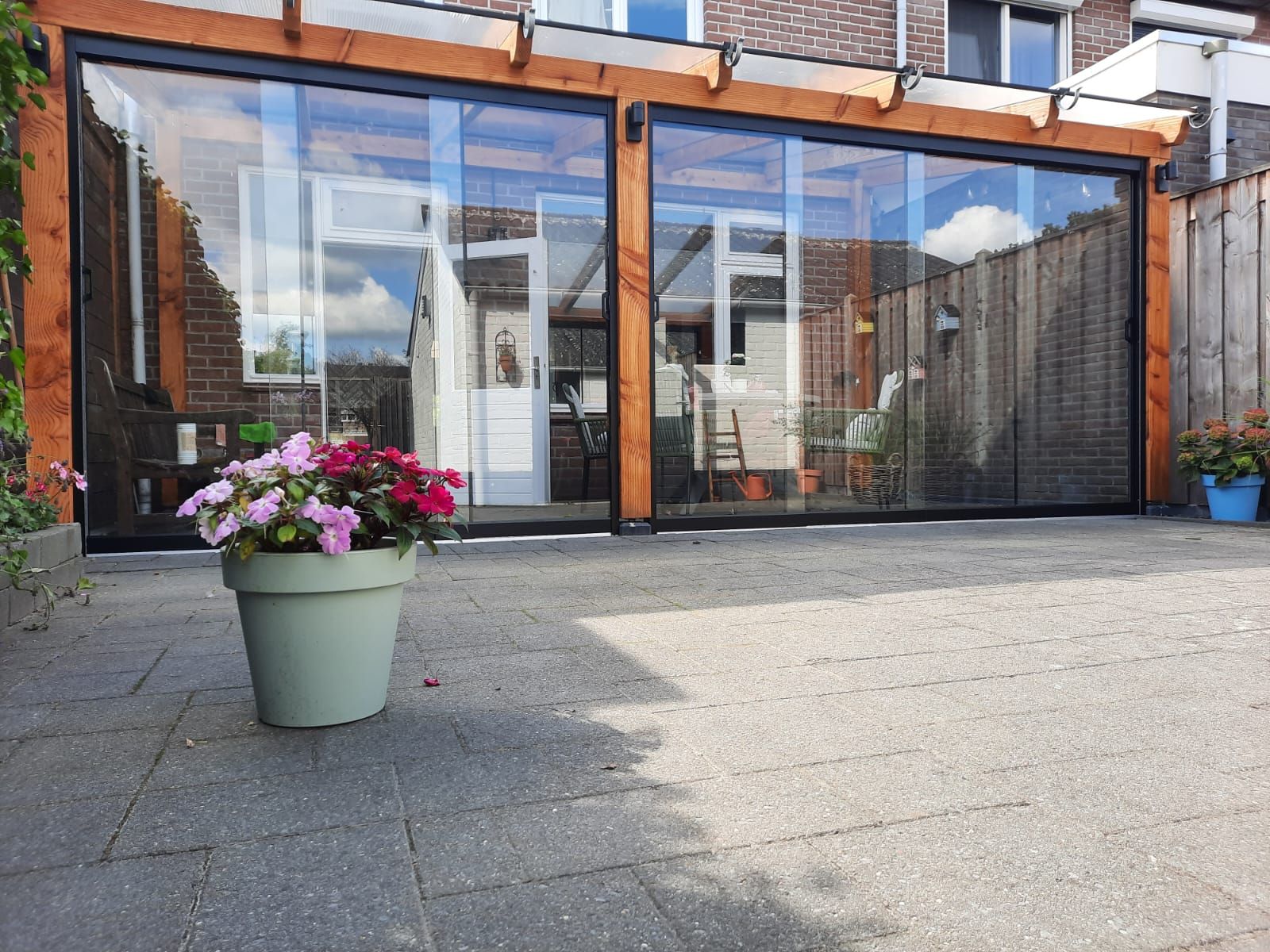 Een pot met bloemen staat voor een grote glazen deur.