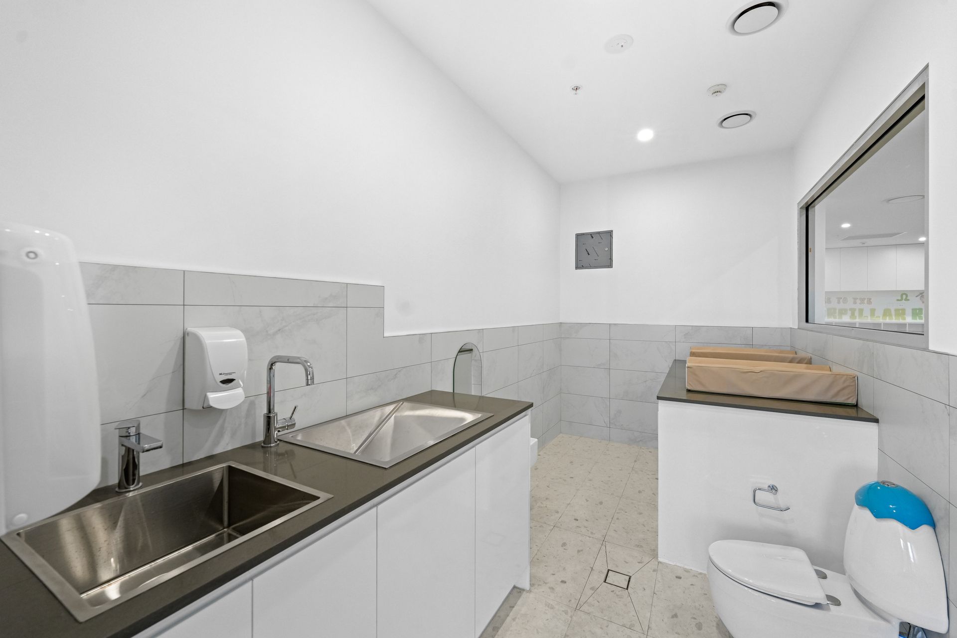 A bright white and gray children toilet with a double sink, toilet, and changing table.